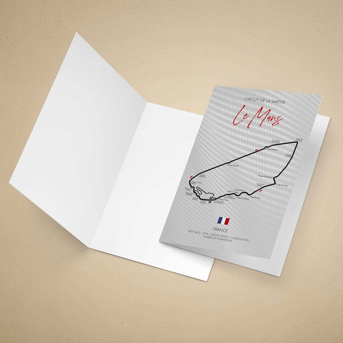 A printed greeting card featuring a black race track map of Le Mans with the text 'Circuit de la Sarte Le Mans' and 'France' at the bottom, standing upright on a warm beige background.