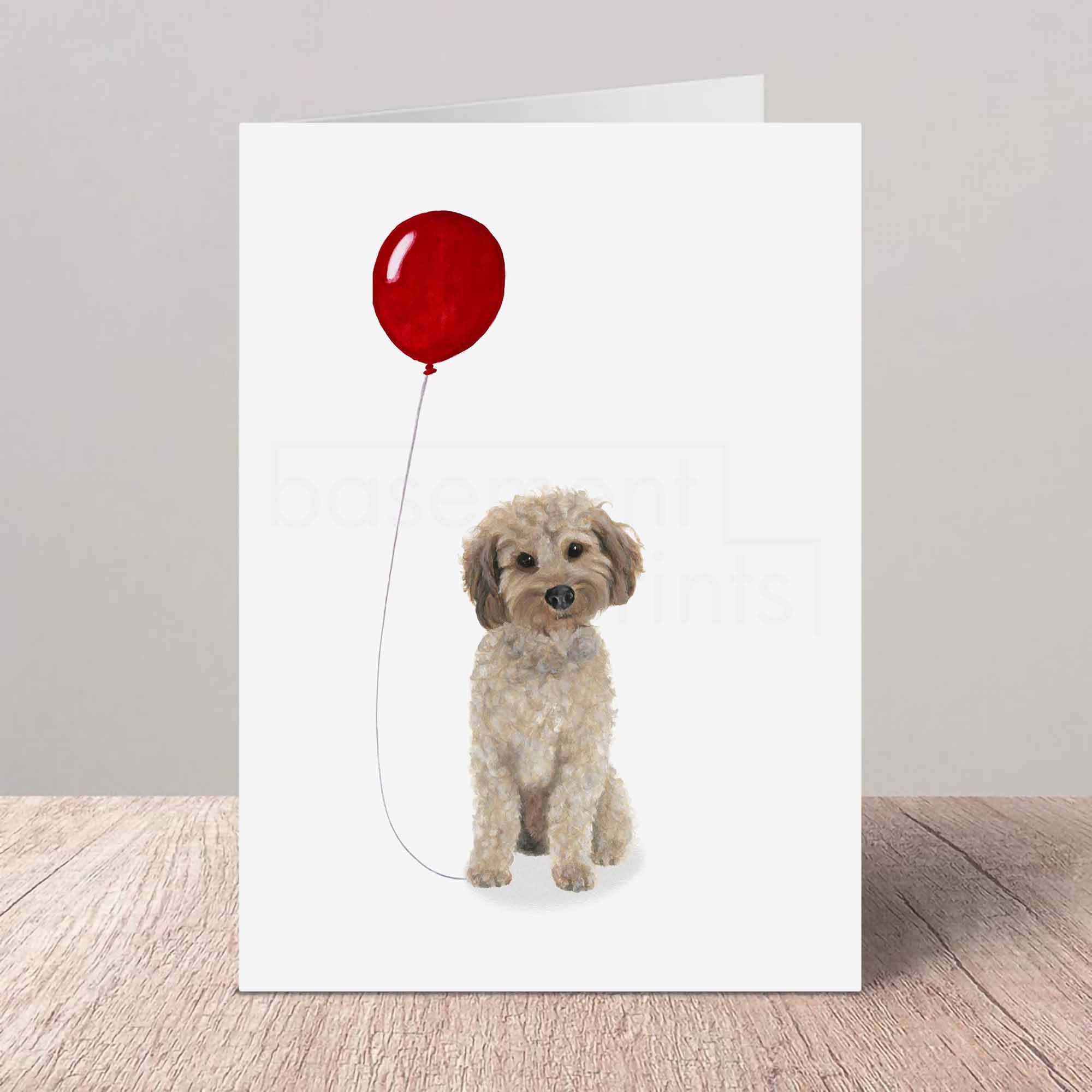 Greeting card with a light brown Cockapoo holding a red balloon on a white background