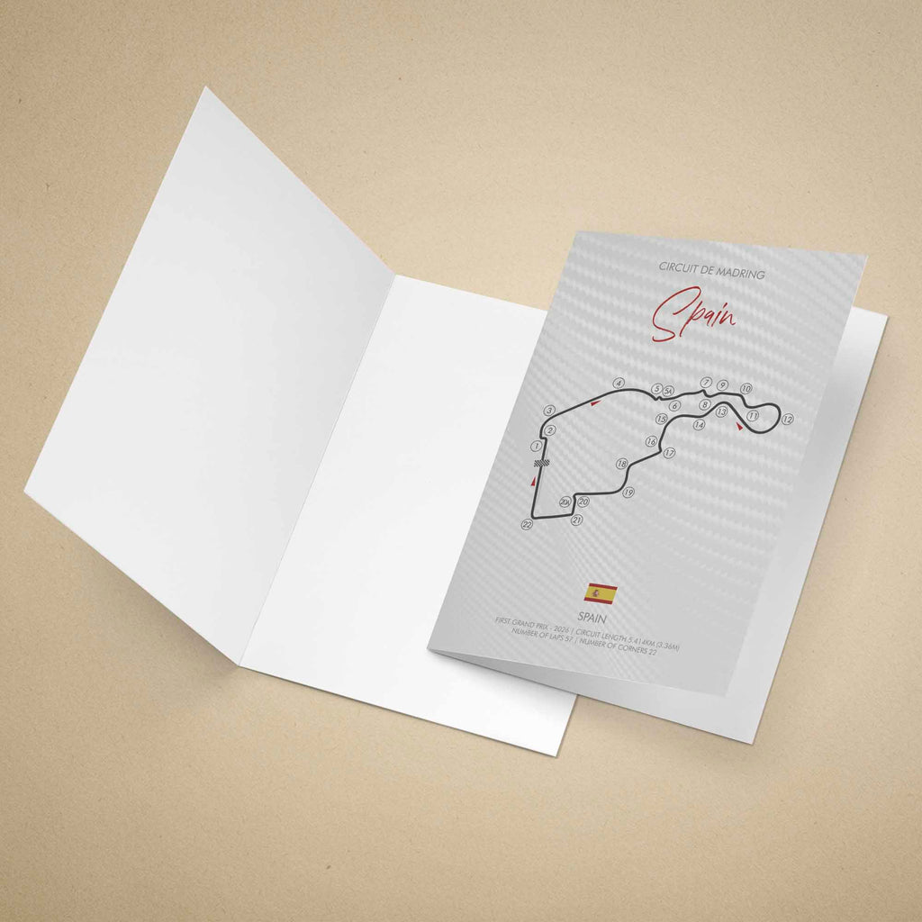 A greeting card set on a warm beige background, with the front cover showing a printed circuit map labeled 'Circuit de Madring Spain' and a small Spanish flag.