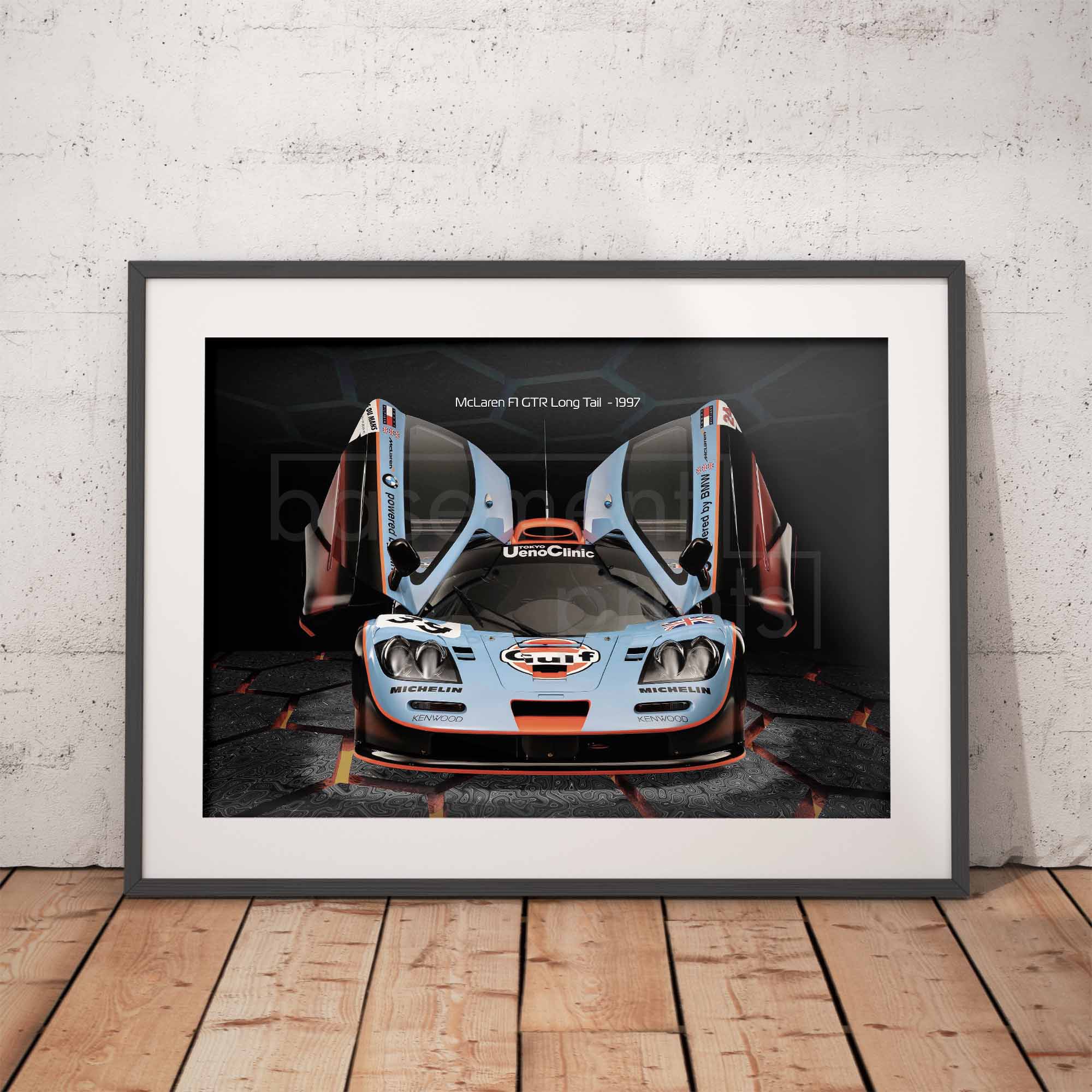 Framed poster of a McLaren F1 GTR Gulf racing car on a white wall with wooden floor.