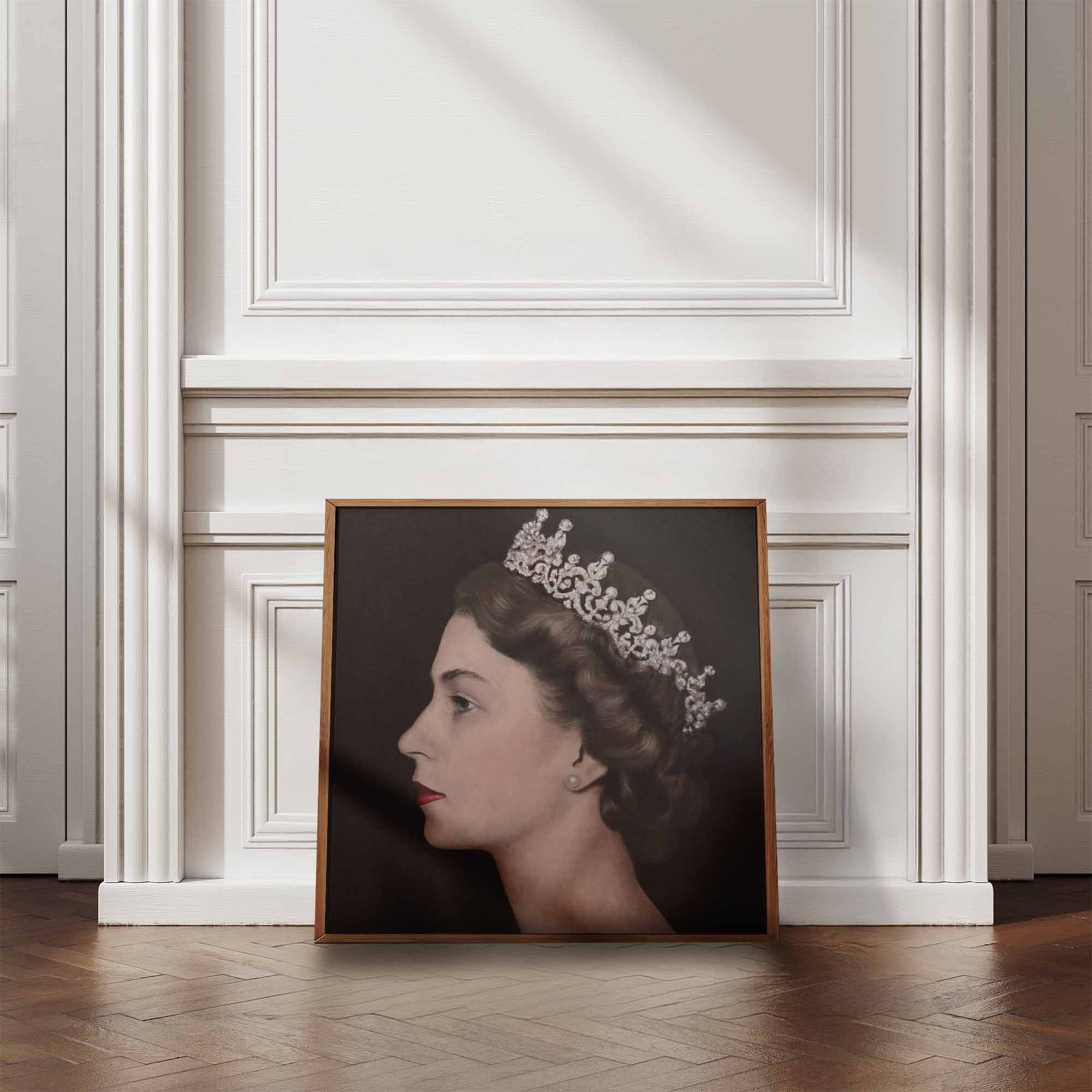 Framed portrait of Queen Elizabeth II wearing a crown on a wall in a room with wooden flooring and white walls.