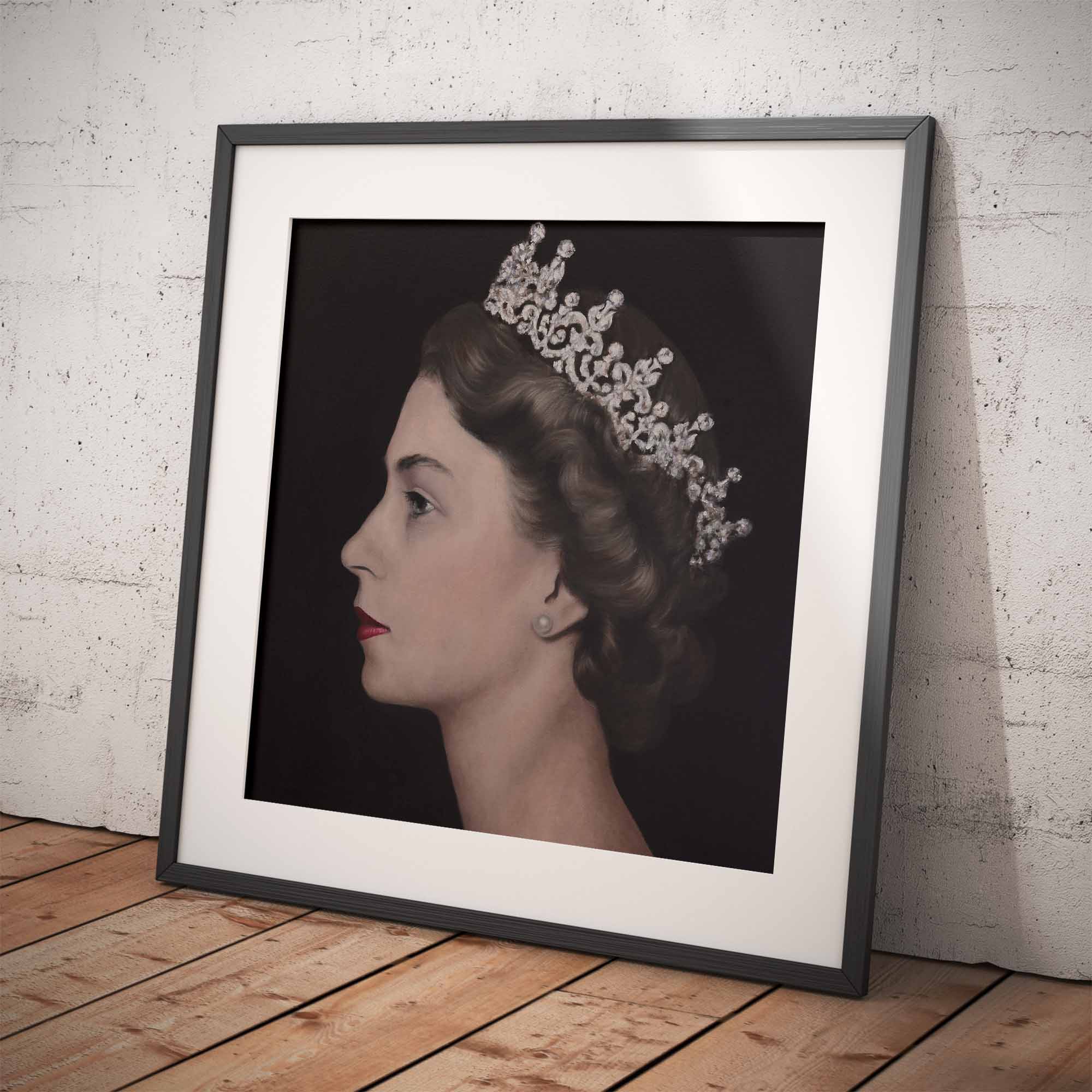 Framed portrait of Queen Elizabeth II wearing a crown on a wooden floor with a white brick wall background