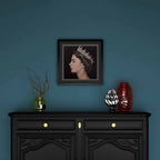 Framed artwork of Queen Elizabeth II above a black cabinet with decorative items against a blue wall