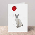 Greeting card with a cat holding a red balloon on a white background