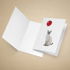 Greeting card with a cat holding a red balloon on a beige background