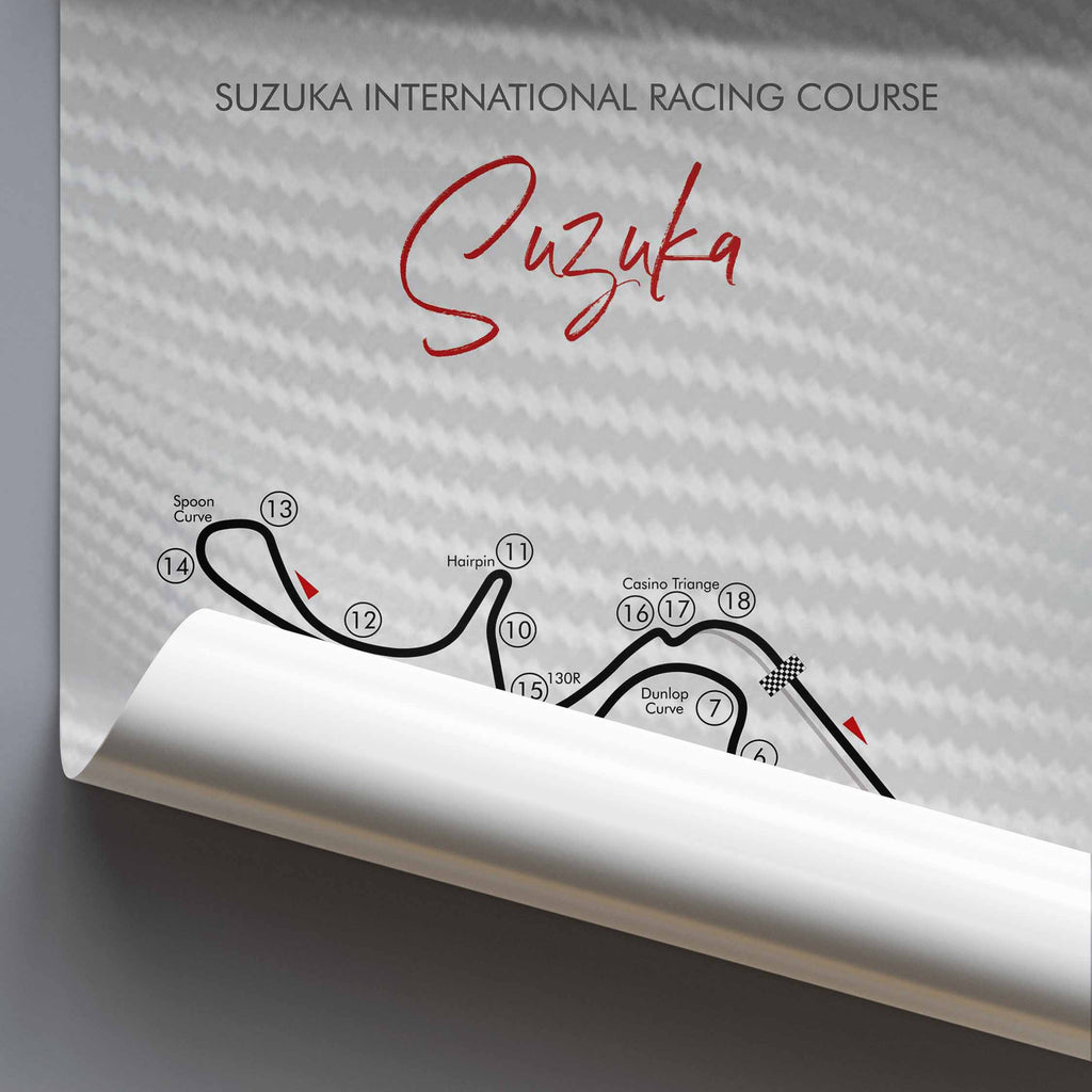 A rolled poster displaying a printed Suzuka International Racing Course map and track layout on a light gray background with a carbon-fiber texture.