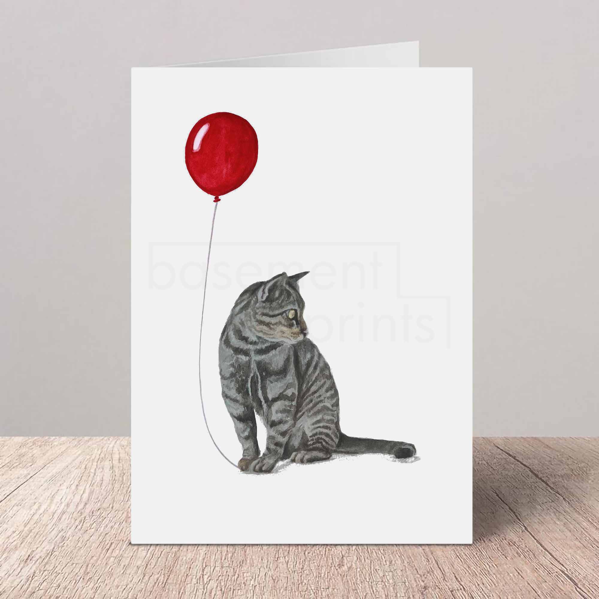 Greeting card with a grey tabby cat and red balloon design on a white background
