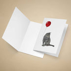Greeting card with a grey tabby cat and red balloon design on a beige background