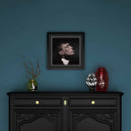 Framed portrait of Thomas Shelby above a black cabinet with decorative items against a blue wall