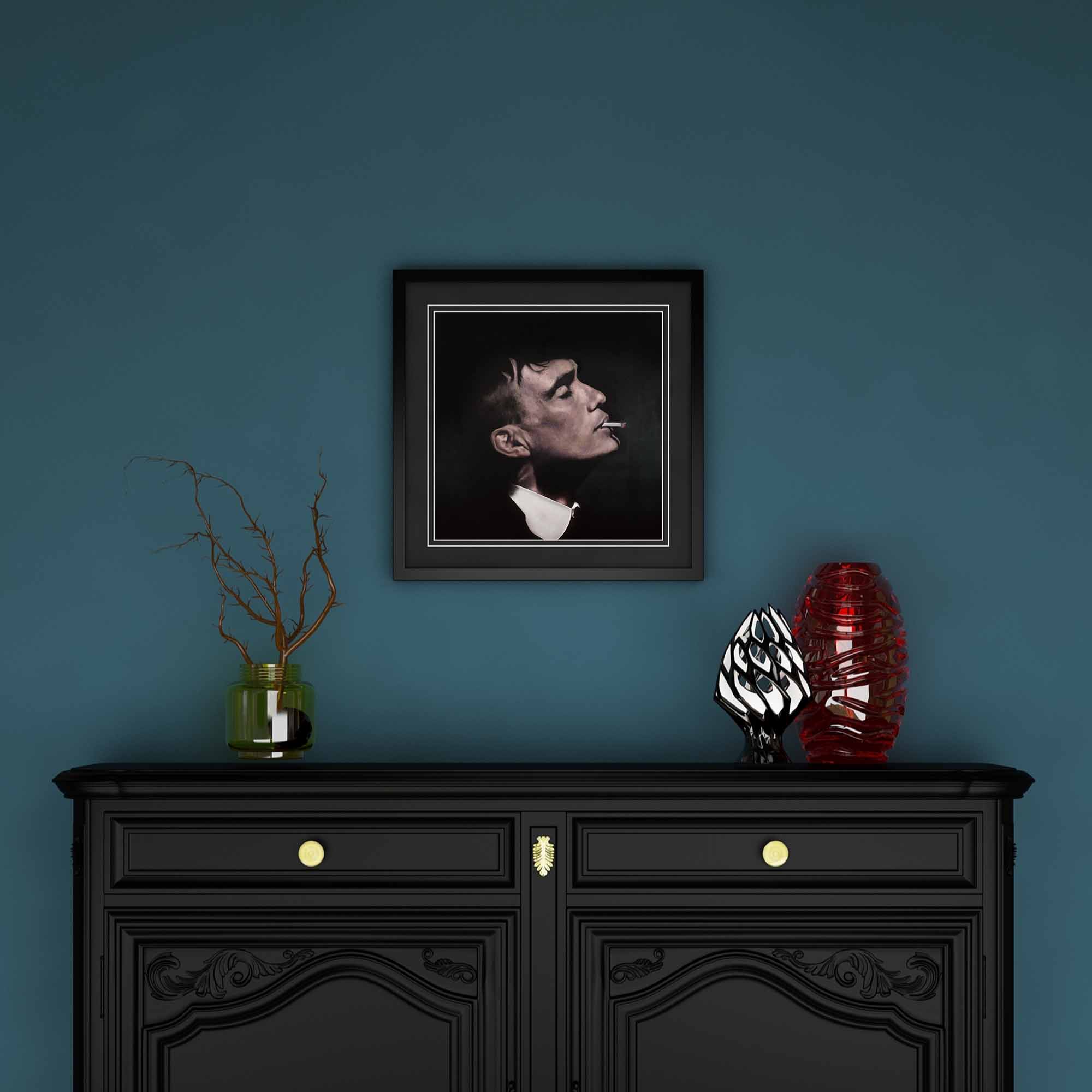 Framed portrait of Thomas Shelby above a black cabinet with decorative items against a blue wall