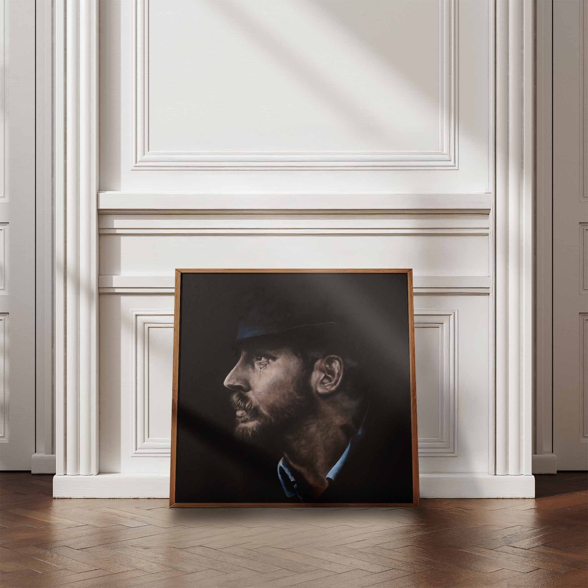 Framed portrait of Tom Hardy on a wall in a room with wooden flooring and white walls.