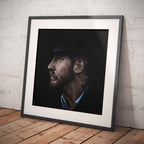 Framed portrait of a Tom Hardy on a wooden floor against a white brick wall.