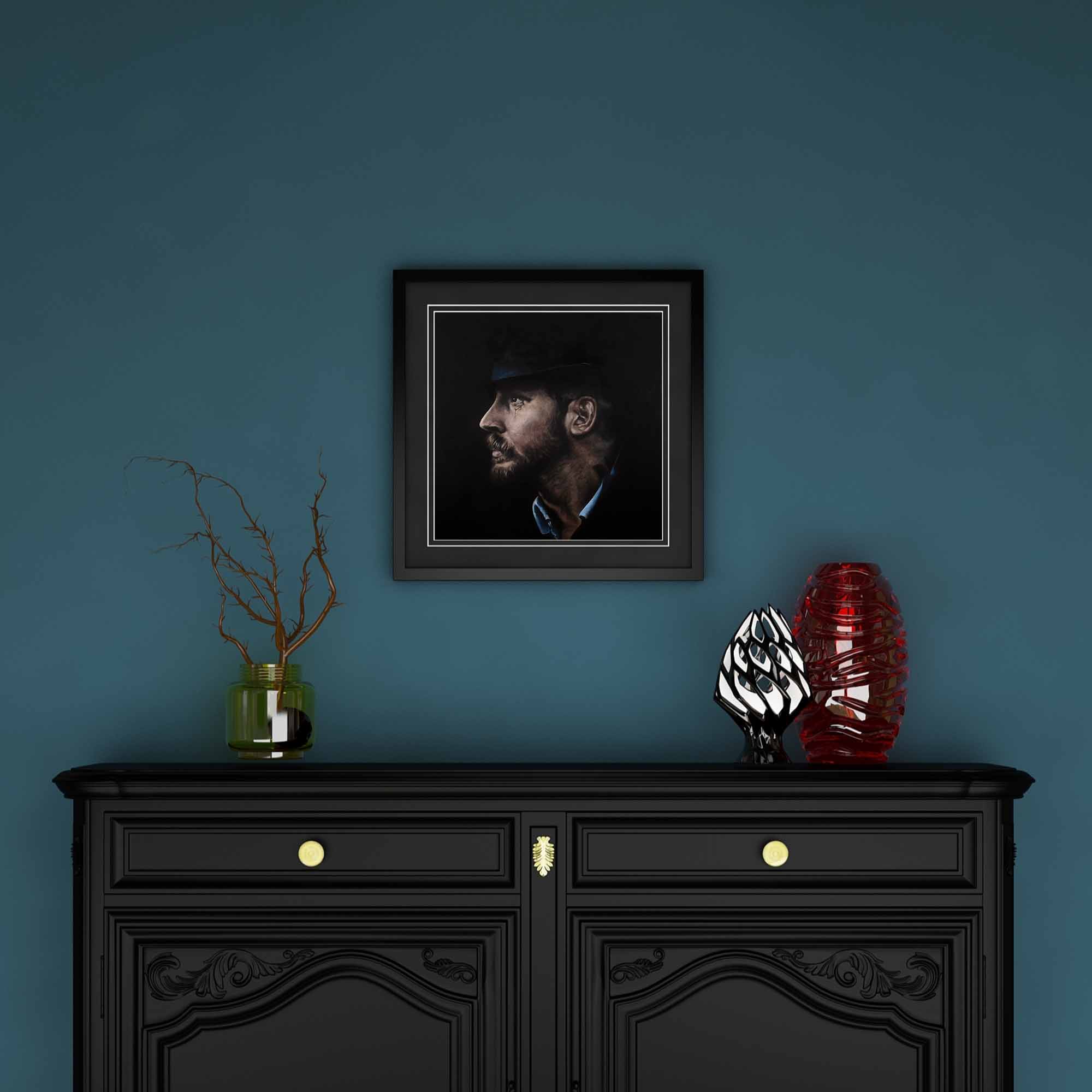 Framed portrait of Tom Hardy above a black cabinet with decorative items against a blue wall
